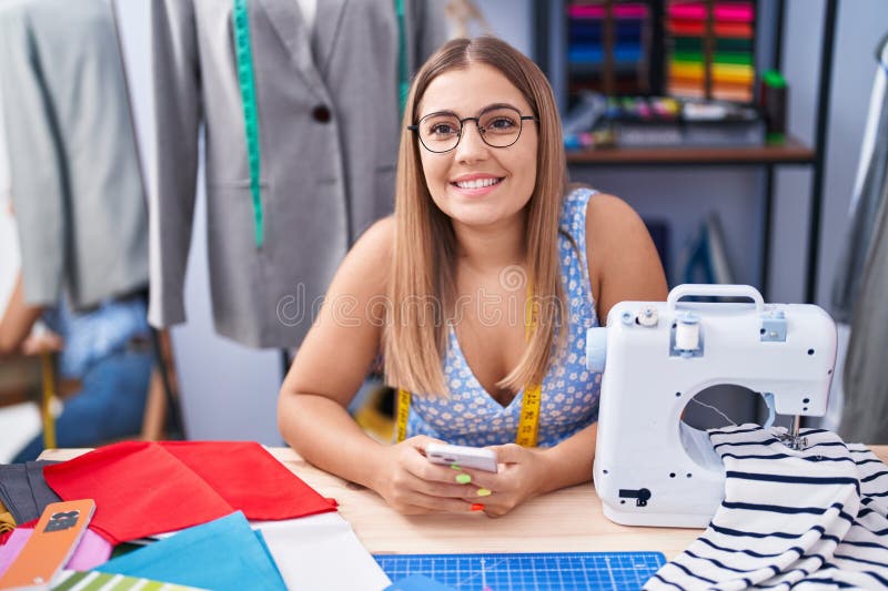 Young beautiful hispanic woman tailor smiling confident using smartphone at tailor shop stock image