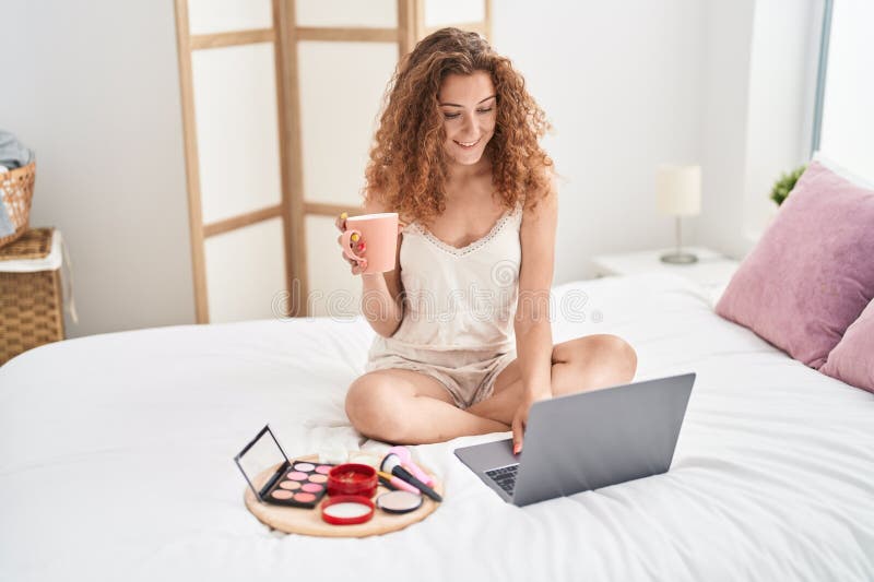 Young beautiful hispanic woman using laptop and drinking coffee at bedroom stock image
