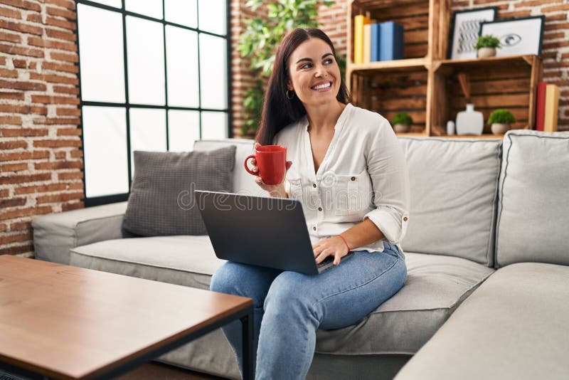 Young beautiful hispanic woman using laptop drinking coffee at home