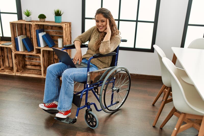 Young beautiful hispanic woman using laptop sitting on wheelchair at home