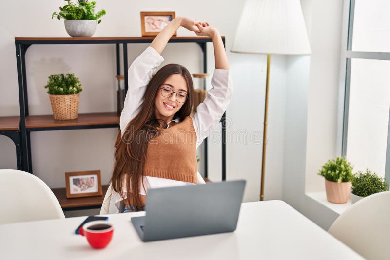 Young beautiful hispanic woman using laptop stretching arms at home