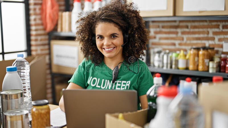 Young beautiful hispanic woman volunteer smiling confident using laptop and headphones at charity center