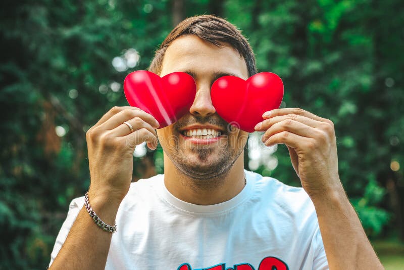 Young beautiful man close up holds the red hearts in his hands instead the eyes