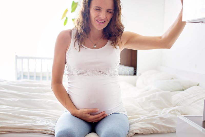 Joven hermoso una mujer, en dolor trabajar contracciones, sobre el una cama en dormitorio, preparación sobre el dar nacimiento.