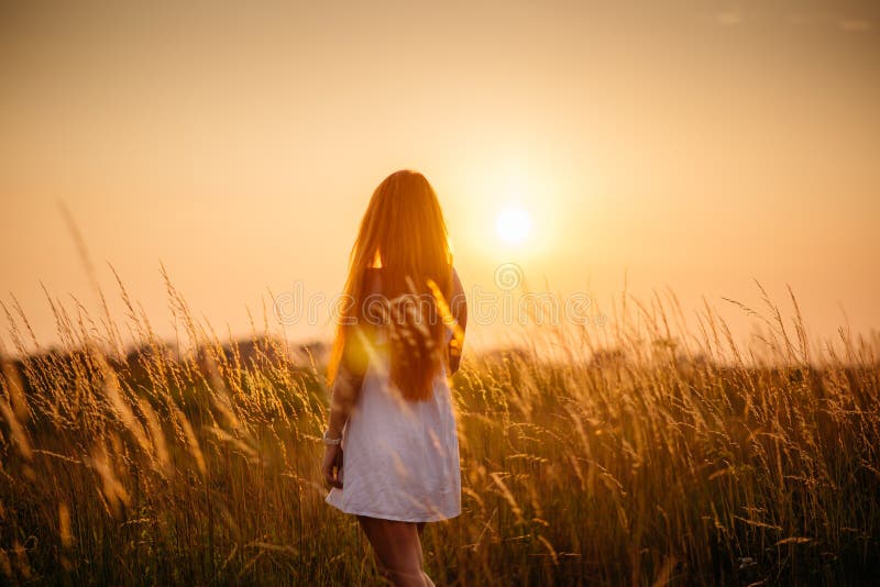 Young beautiful red-haired girl in a field at sunset