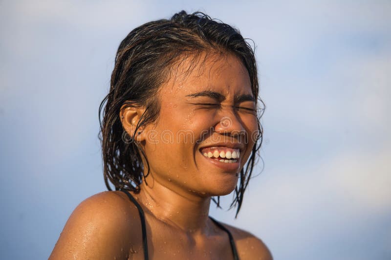 Young beautiful and sexy Asian girl in bikini with wet hair enjoying holidays at tropical beach posing cool laughing happy at the