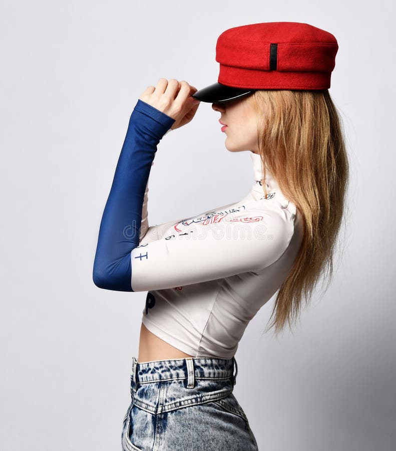Young beautiful slim blond woman in longsleeve, jeans and red cap standing side ways and holding headdress