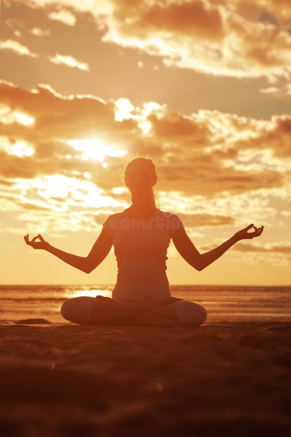 Young beautiful slim woman silhouette practices yoga on the beach at sunset. Yoga at sunrise