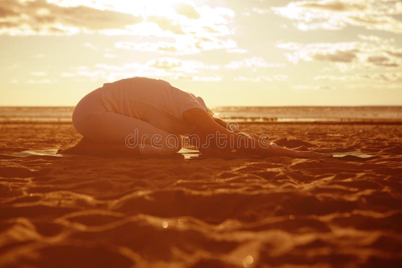 Young beautiful slim woman silhouette practices yoga on the beach at sunrise. Yoga at sunset