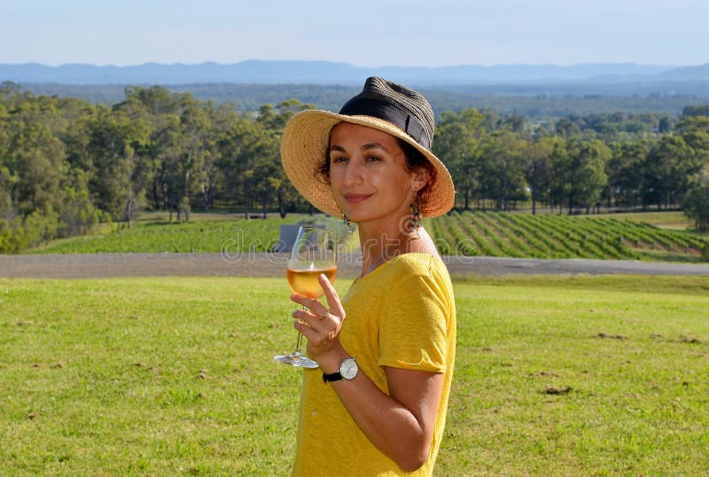 A young beautiful smiling woman wearing a hat and holding a glass cold white wine royalty free stock image