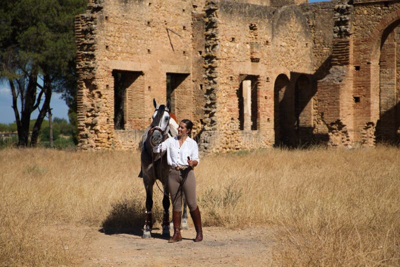 Young and beautiful Spanish woman with her thoroughbred horse. The woman is wearing a riding uniform and looks with love and