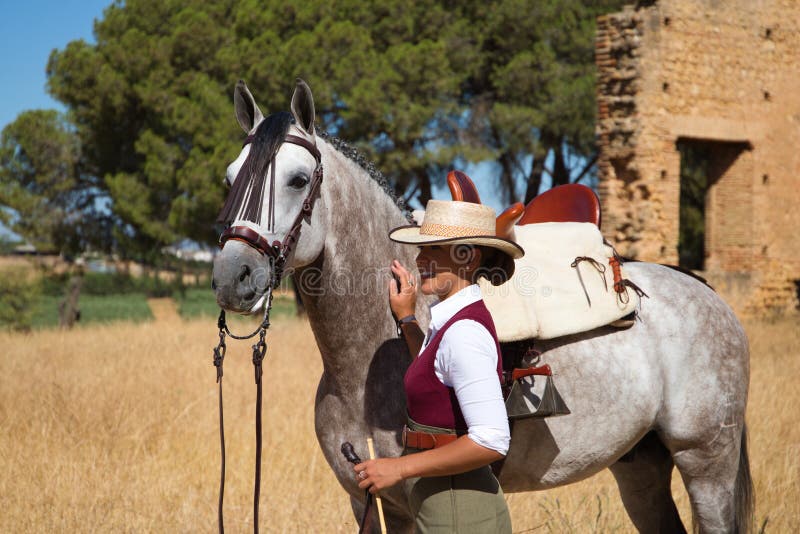 Young and beautiful Spanish woman with her thoroughbred horse. The woman is wearing a riding uniform and a typical Spanish hat.