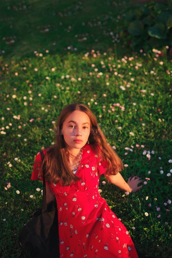 Young beautiful teen girl in red dress is resting on fresh spring grass