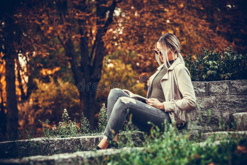 Young beautiful urban woman is reading book while sitting in the