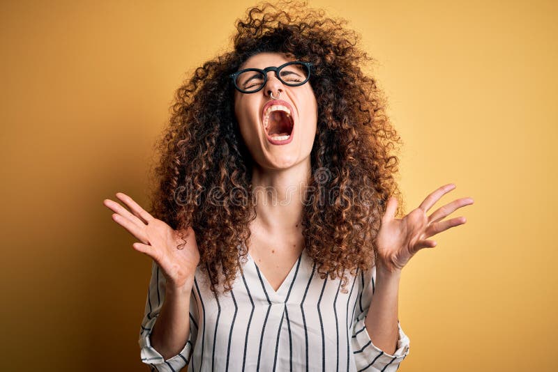 Young beautiful woman with curly hair and piercing wearing striped shirt and glasses celebrating mad and crazy for success with