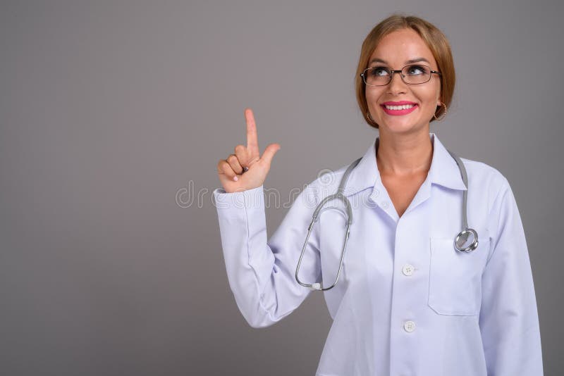 Young Beautiful Woman Doctor With Blond Hair Against Gray Backgr Stock