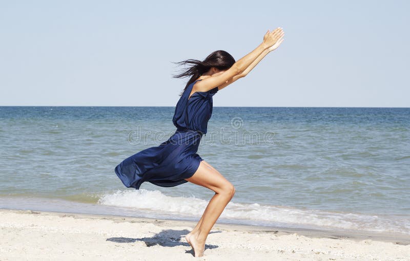 Young beautiful woman doing yoga at seaside in blue dress