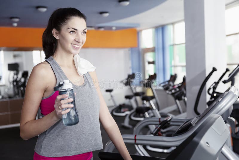 Young beautiful woman drinks water on the treadmill in the gym stock image Young beautiful woman drinks water on the treadmill in the gym stock image