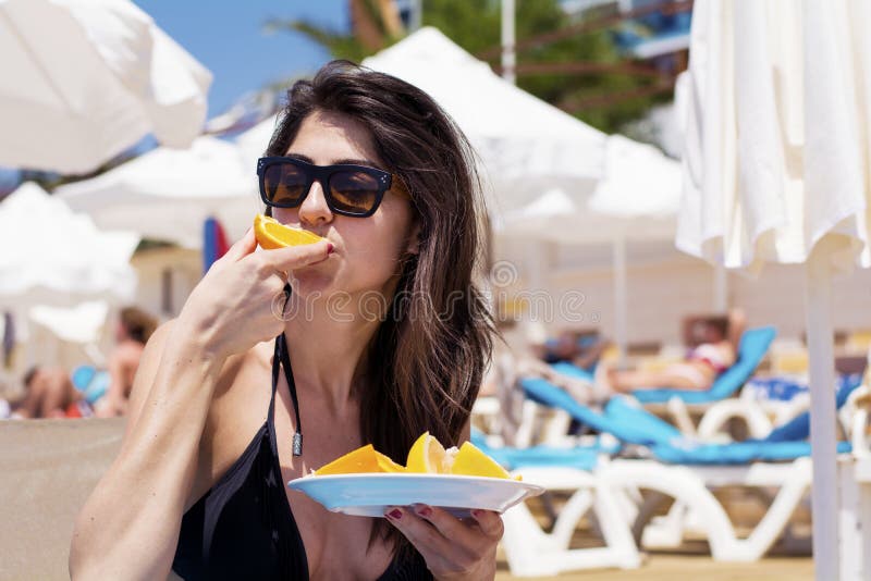 Young beautiful woman eating fresh orange fruit at the beach stock photo Young beautiful woman eating fresh orange fruit at the beach stock photo