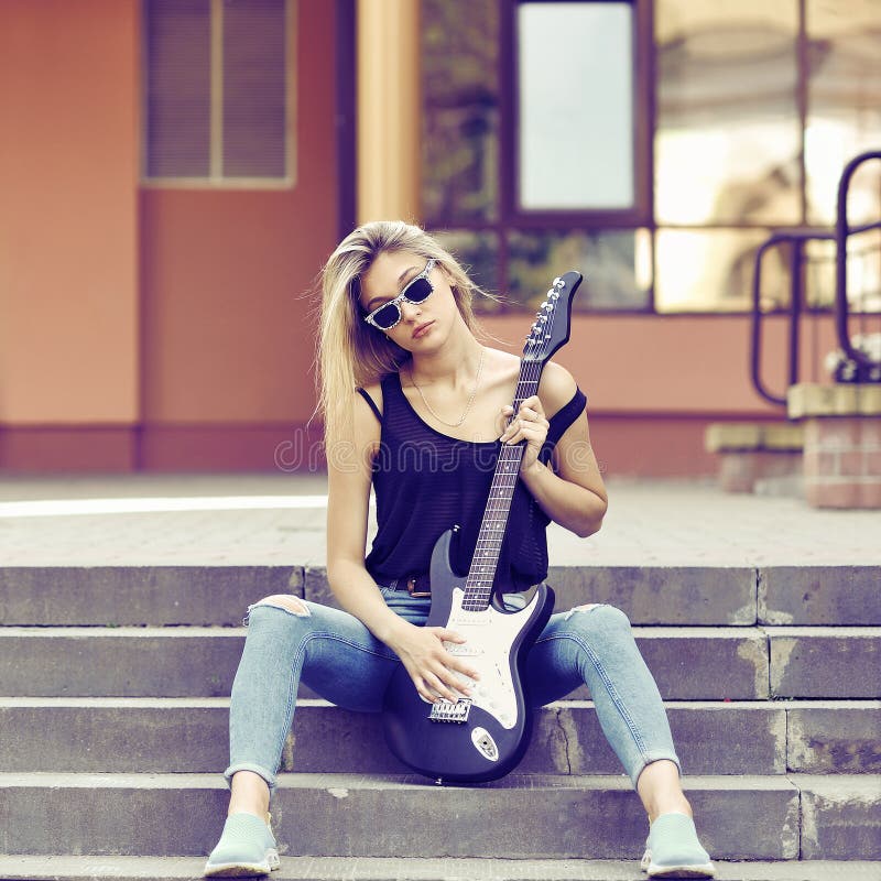 Young beautiful woman with electric guitar wearing sunglasses