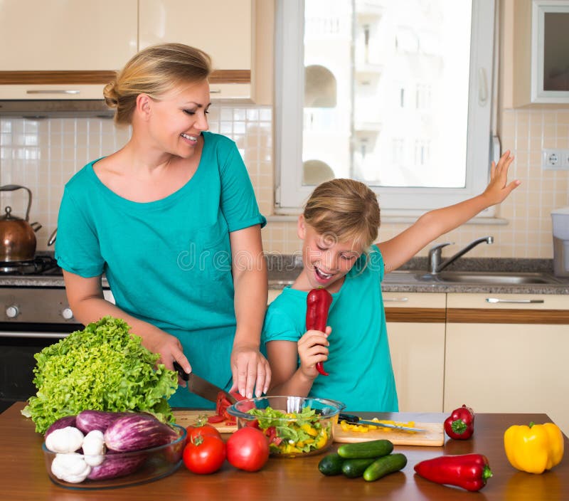 Young beautiful women and girl making fresh vegetable salad. Healthy domestic food concept. Smiling mother and funny playful daughter cooking together, help children to parents. Young beautiful women and girl making fresh vegetable salad. Healthy domestic food concept. Smiling mother and funny playful daughter cooking together, help children to parents.