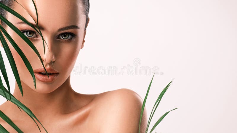 Young beautiful woman with green leaves near naked body. Body care beauty treatments concept.  Girl`s  face with green flowers