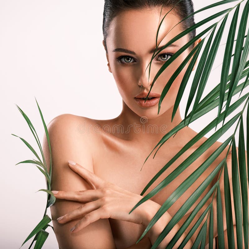 Young beautiful woman with green leaves near naked body. Body care beauty treatments concept.  Girl`s  face with green flowers