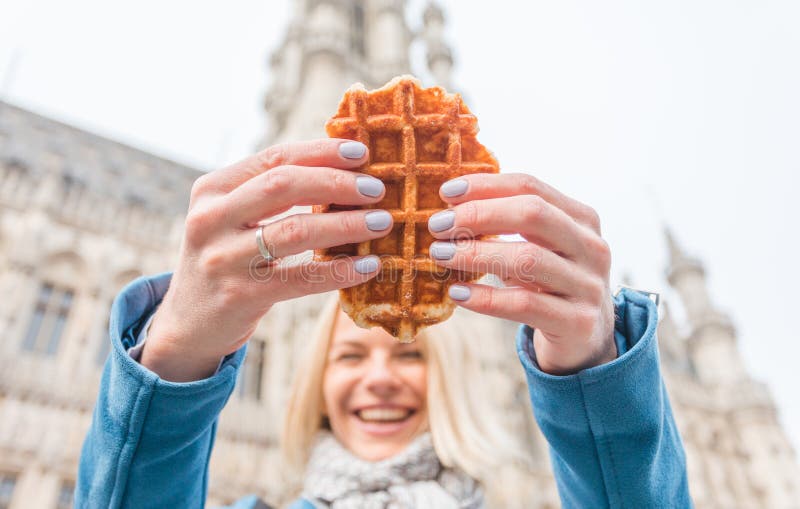 Young beautiful woman holding a traditional Belgian waffle on the background of the Great Market Square in Brussels