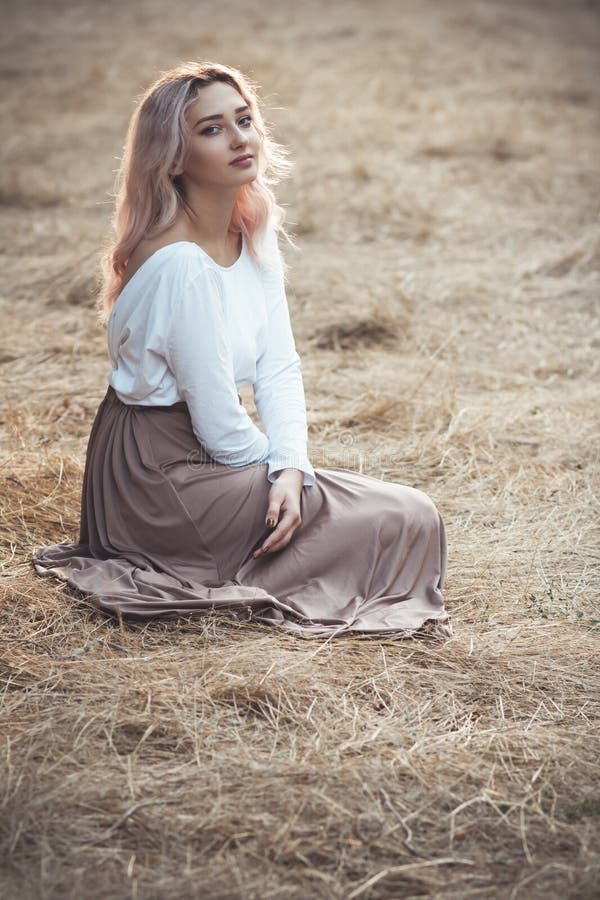 Young beautiful woman in a long dress on a background of dry grass sitting on glade in the forest, romantic girl relaxing alone in royalty free stock photography Young beautiful woman in a long dress on a background of dry grass sitting on glade in the forest, romantic girl relaxing alone in royalty free stock photography