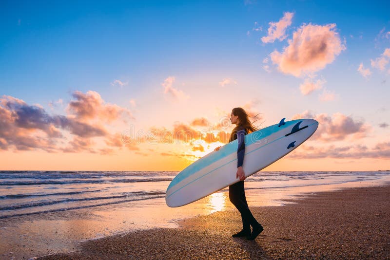 Young beautiful woman with long hair. Surf girl with surfboard on a beach at sunset or sunrise. Surfer and ocean royalty free stock photo Young beautiful woman with long hair. Surf girl with surfboard on a beach at sunset or sunrise. Surfer and ocean royalty free stock photo