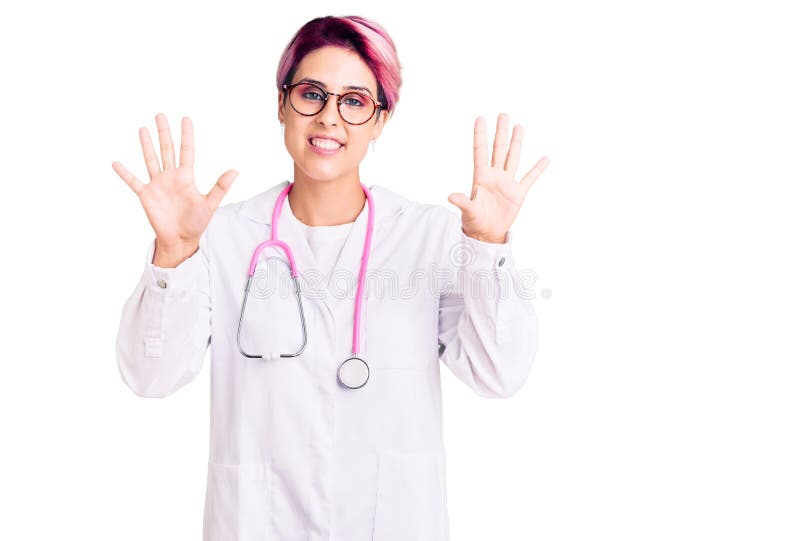 Young beautiful woman with pink hair wearing doctor uniform showing and pointing up with fingers number ten while smiling confident and happy
