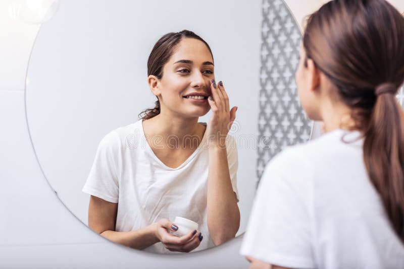 Young beautiful woman putting face cream on her nice healthy skin