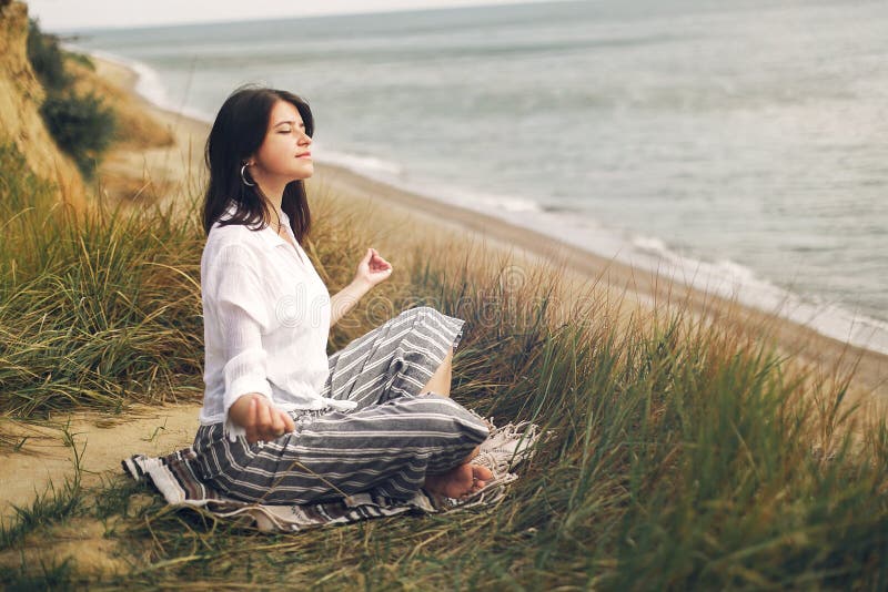Young beautiful woman relaxing and practicing yoga on beach, sitting in grass and sand, meditating and listening to sea waves. royalty free stock photography Young beautiful woman relaxing and practicing yoga on beach, sitting in grass and sand, meditating and listening to sea waves. royalty free stock photography