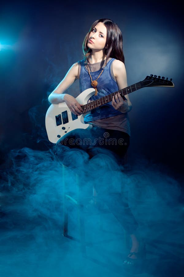 Young beautiful woman is sitting on stage with a guitar . Fog on