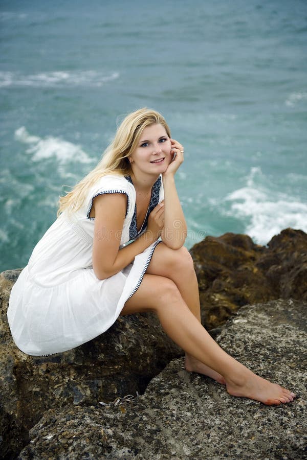 Young beautiful woman sitting on a stone near sea