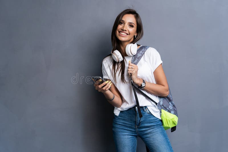 Young beautiful woman with smart phone. Smiling student girl going on a travel. Isolated on gray background. stock photography