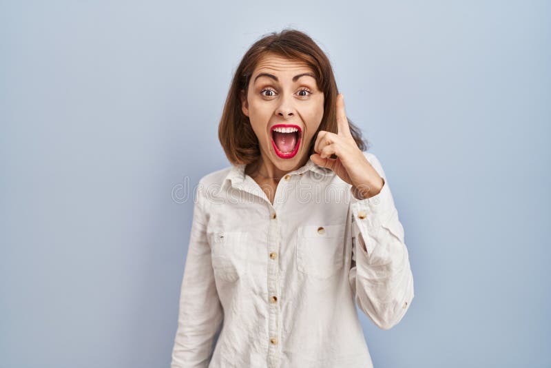 Young beautiful woman standing casual over blue background pointing finger up with successful idea