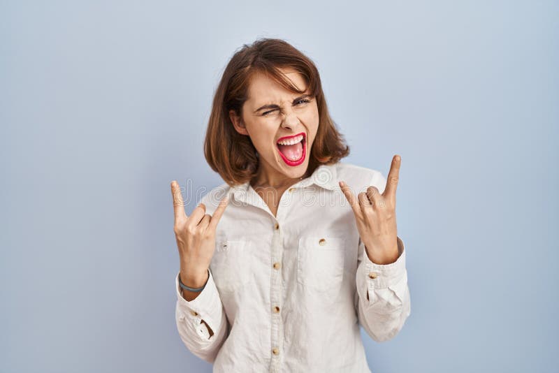 Young beautiful woman standing casual over blue background shouting with crazy expression doing rock symbol with hands up