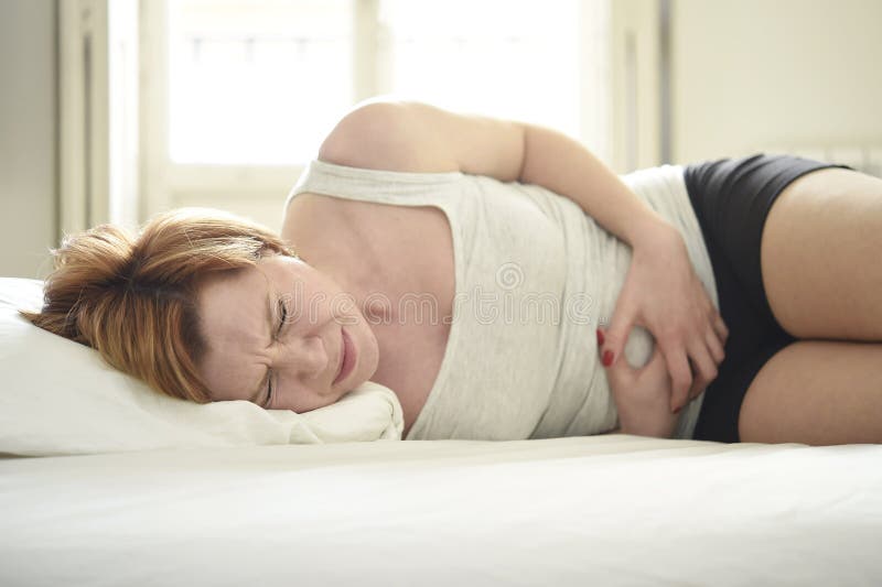 Young beautiful woman suffering stomach cramps on belly holding tummy with her hands in period pain