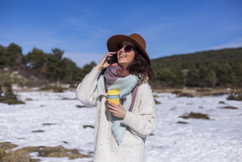 Young beautiful woman talking on her mobile phone in the snow and holding a cup of tea or coffee. Outdoors portrait, lifestyle stock images Young beautiful woman talking on her mobile phone in the snow and holding a cup of tea or coffee. Outdoors portrait, lifestyle stock images