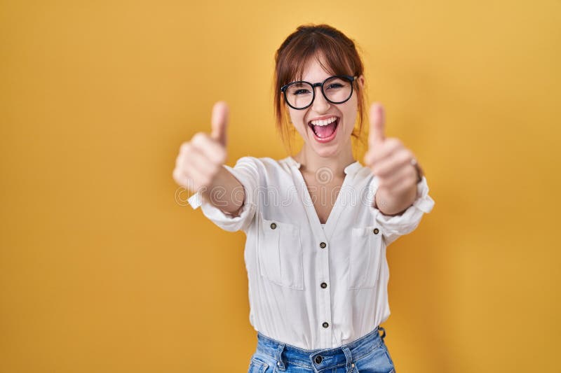 Young beautiful woman wearing casual shirt over yellow background approving doing positive gesture with hand, thumbs up smiling