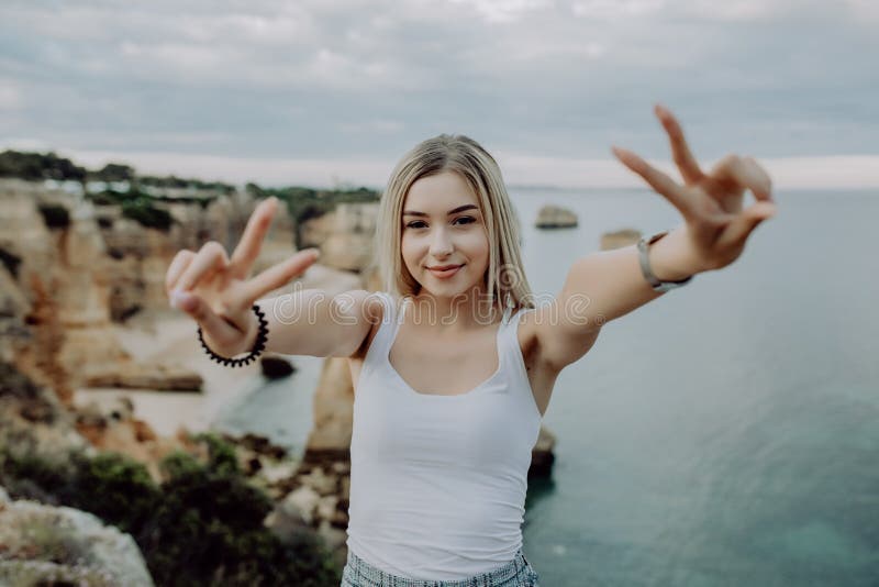 Young woman with victory gesture on beauty landscape of ocean rocky beach