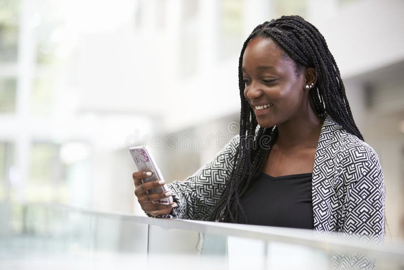 Young black female student using phone in university foyer royalty free stock photography
