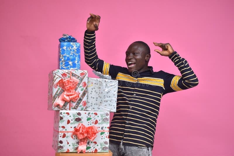 young black man feeling excited and happy and delighted, celebrating while standing next to a stack of gift boxes with fists in royalty free stock photos young black man feeling excited and happy and delighted, celebrating while standing next to a stack of gift boxes with fists in royalty free stock photos