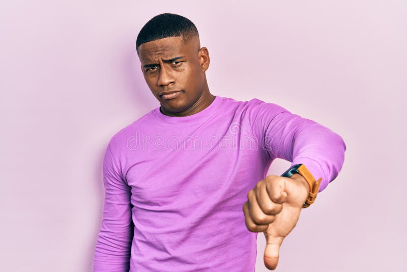 Young black man wearing casual pink sweater looking unhappy and angry showing rejection and negative with thumbs down gesture