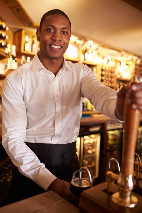 A young black man working behind a bar looks to camera royalty free stock photo