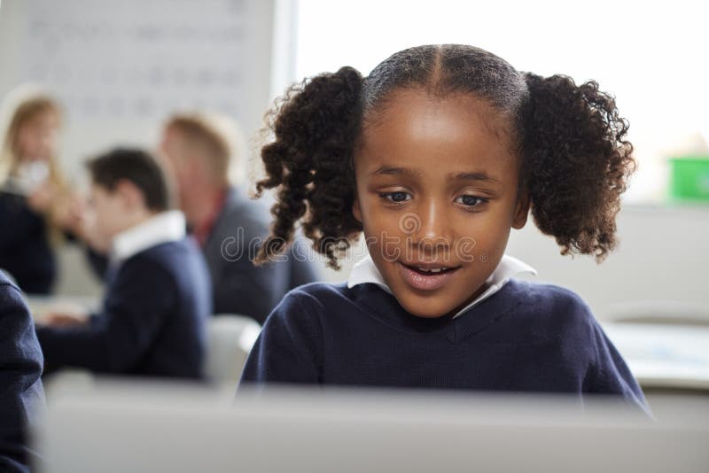 Young black schoolgirl using a laptop computer sitting at desk in a primary school classroom, front view, close up stock photos
