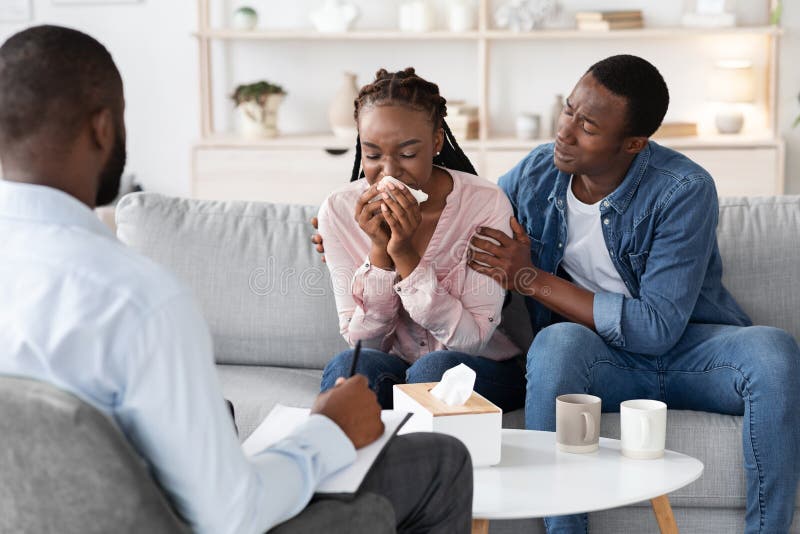 Young black woman crying at meeting with family counselor, caring husband comforting her during couples psychotherapy session, upset african american lady having emotional breakdown, free space. Young black woman crying at meeting with family counselor, caring husband comforting her during couples psychotherapy session, upset african american lady having emotional breakdown, free space