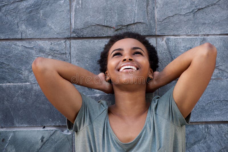 Young black woman laughing against gray wall with hands behind head royalty free stock images Young black woman laughing against gray wall with hands behind head royalty free stock images