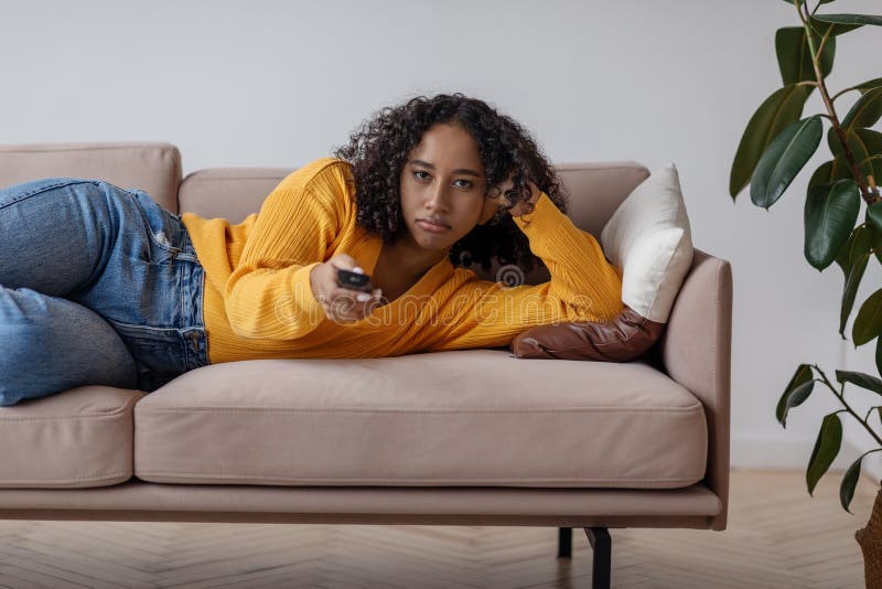 Young Black Woman with Remote Control Lying on Sofa, Feeling Bored ...